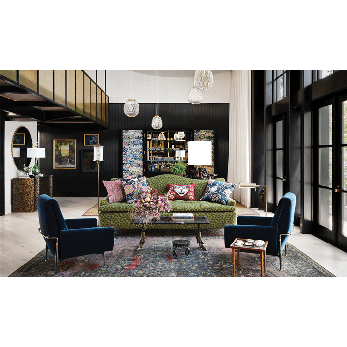 The living space features two blue suede chairs, a colorful green couch, and a unique glass table in the middle.