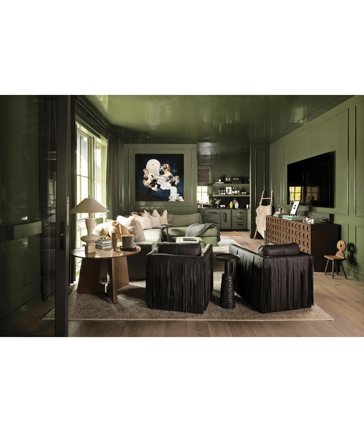 Living area with dark green walls, an art piece hanging on the back wall, brown chairs, and a section sofa.