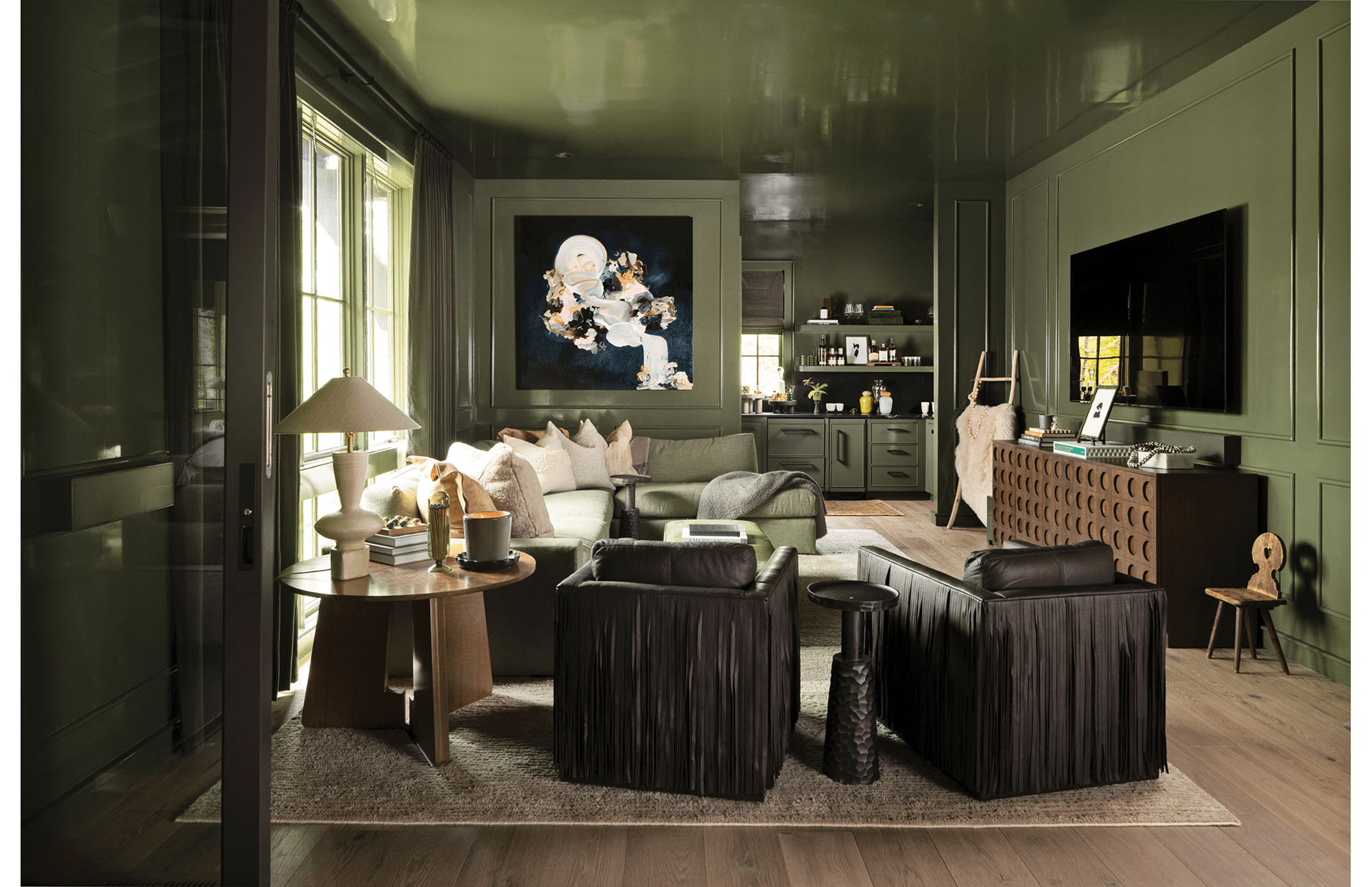 Living area with dark green walls, an art piece hanging on the back wall, brown chairs, and a section sofa.
