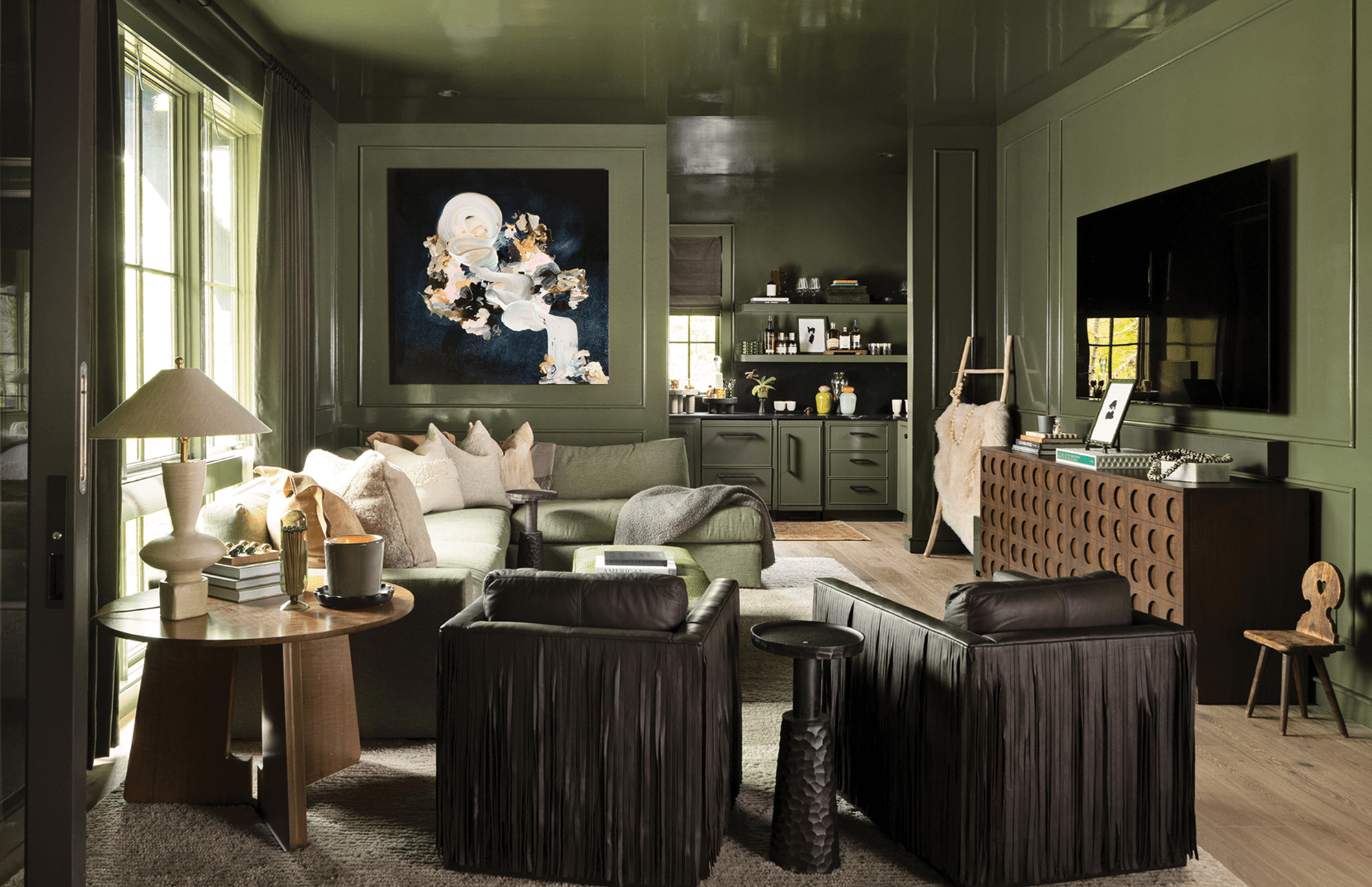 Living area with dark green walls, an art piece hanging on the back wall, brown chairs, and a section sofa.