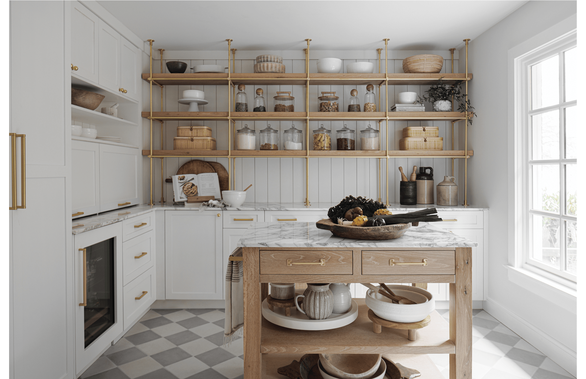 A white marble-colored kitchen featuring a wood-colored table with an assortment of fruits and vegetables on top.