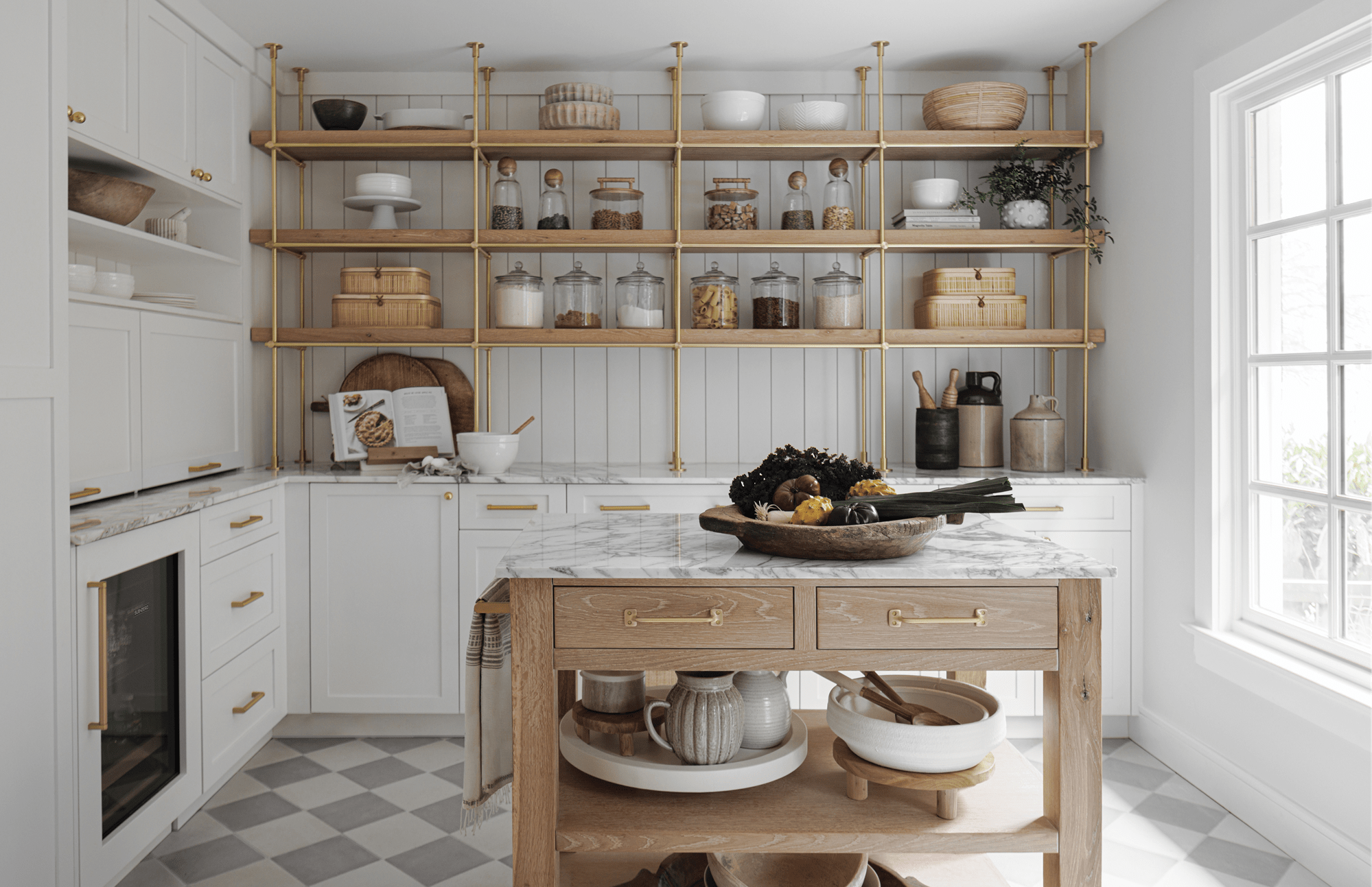 A white marble-colored kitchen featuring a wood-colored table with an assortment of fruits and vegetables on top.