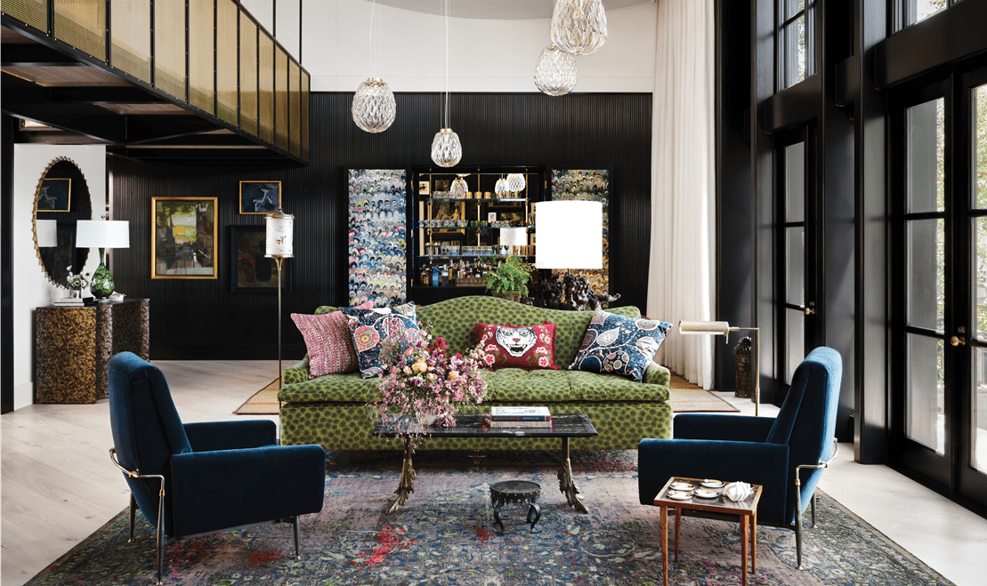 The living space features two blue suede chairs, a colorful green couch, and a unique glass table in the middle.