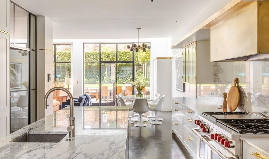 A brass box designed to go around Wolf range hood and a wall of floor-to-ceiling white cabinetry conceals all cookware and the Sub-Zero refrigerator and freezer