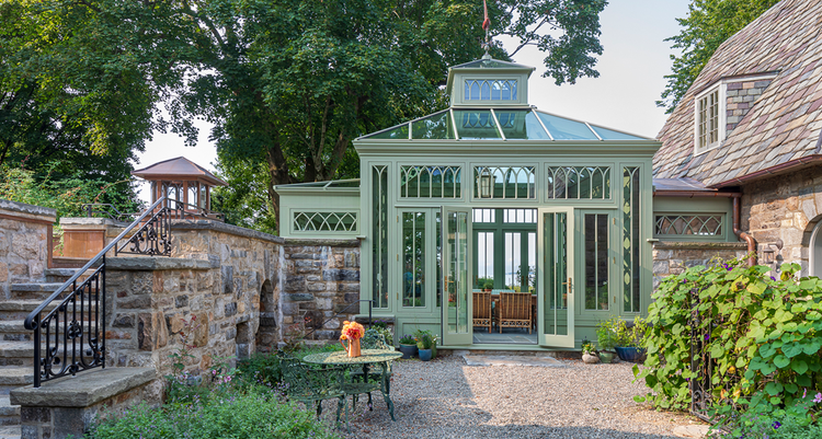 A conservatory in Greenwich, Connecticut, with green siding and large windows next to an aged-brick linkway.