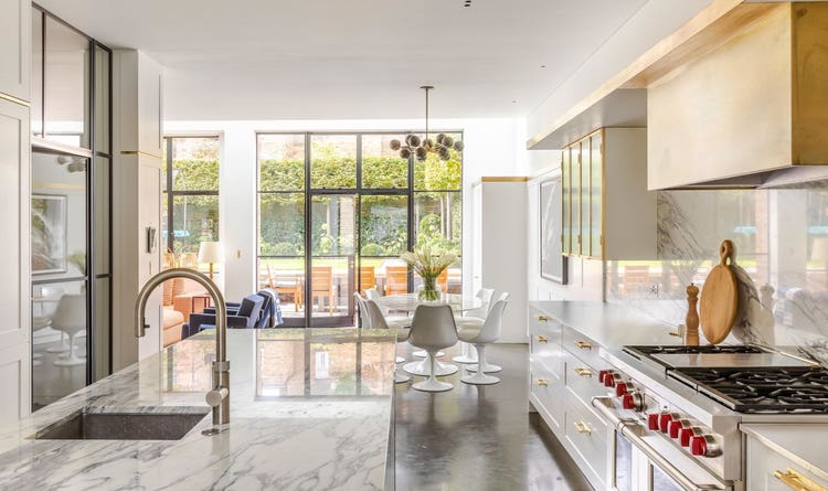 A brass box designed to go around Wolf range hood and a wall of floor-to-ceiling white cabinetry conceals all cookware and the Sub-Zero refrigerator and freezer