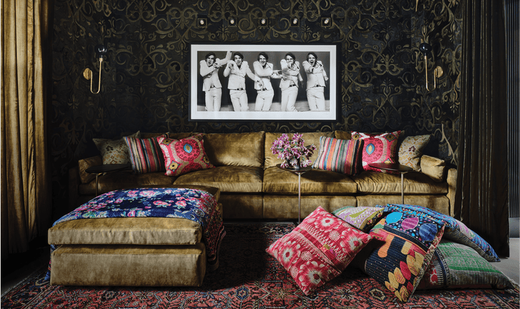 A golden couch with multiple colorful pillows in front of black-and-white artwork depicting Steve Martin in 5 poses.