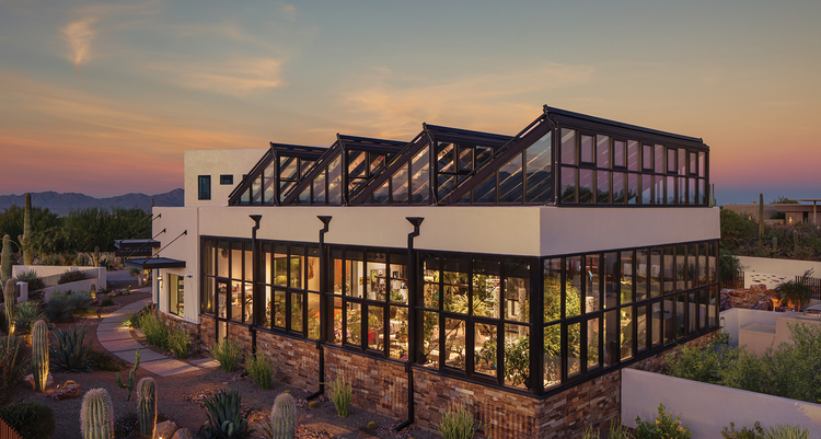 A climate-controlled botanical garden in Tuscon, Arizona with large windows lining the exterior and a brick foundation.