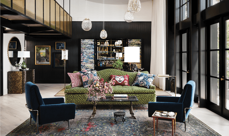 The living space features two blue suede chairs, a colorful green couch, and a unique glass table in the middle.
