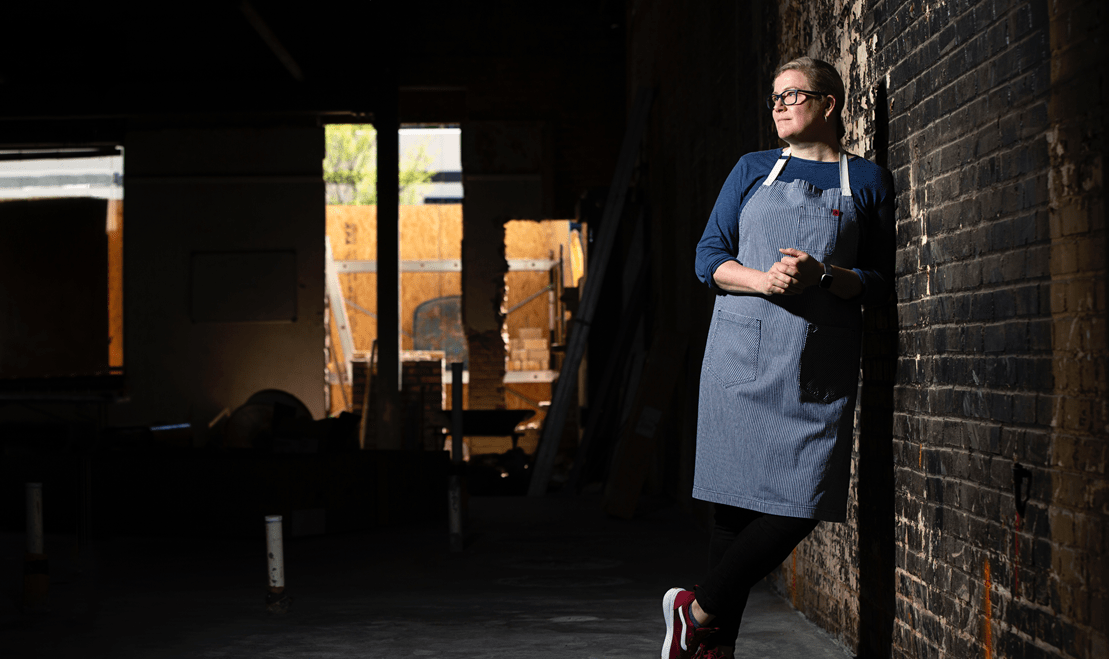 Chef Christensen leaning against a brick wall with her hands together and legs crossed.