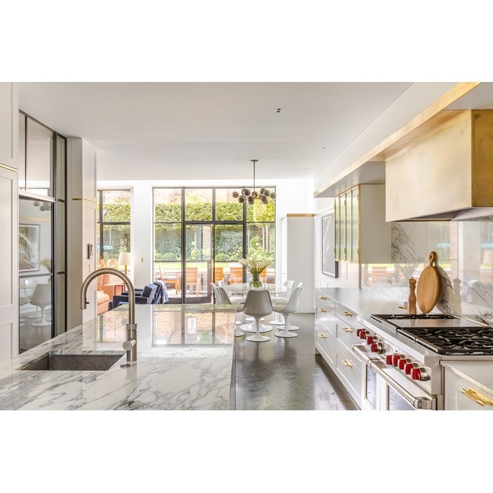A brass box designed to go around Wolf range hood and a wall of floor-to-ceiling white cabinetry conceals all cookware and the Sub-Zero refrigerator and freezer