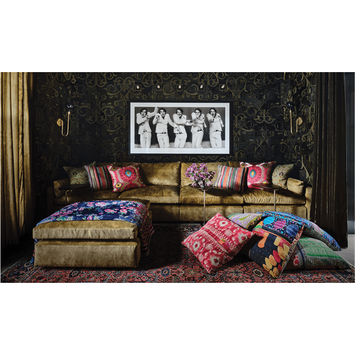 A golden couch with multiple colorful pillows in front of black-and-white artwork depicting Steve Martin in 5 poses.