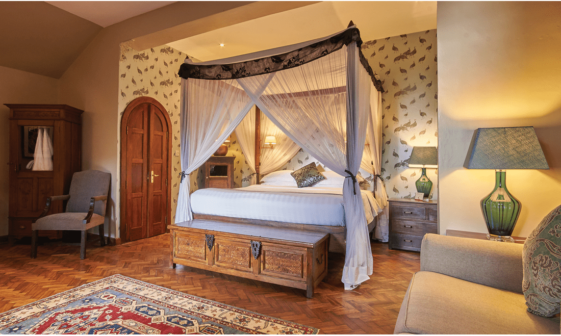 An old-fashioned bedroom with pheasant wallpaper and a cedar chest at the foot of a canopy bed.