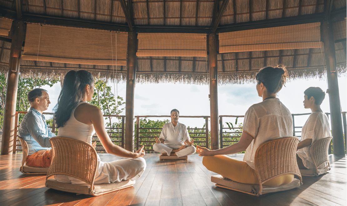 Four students and one teacher sit in a canopy participating in a meditation and yoga session.
