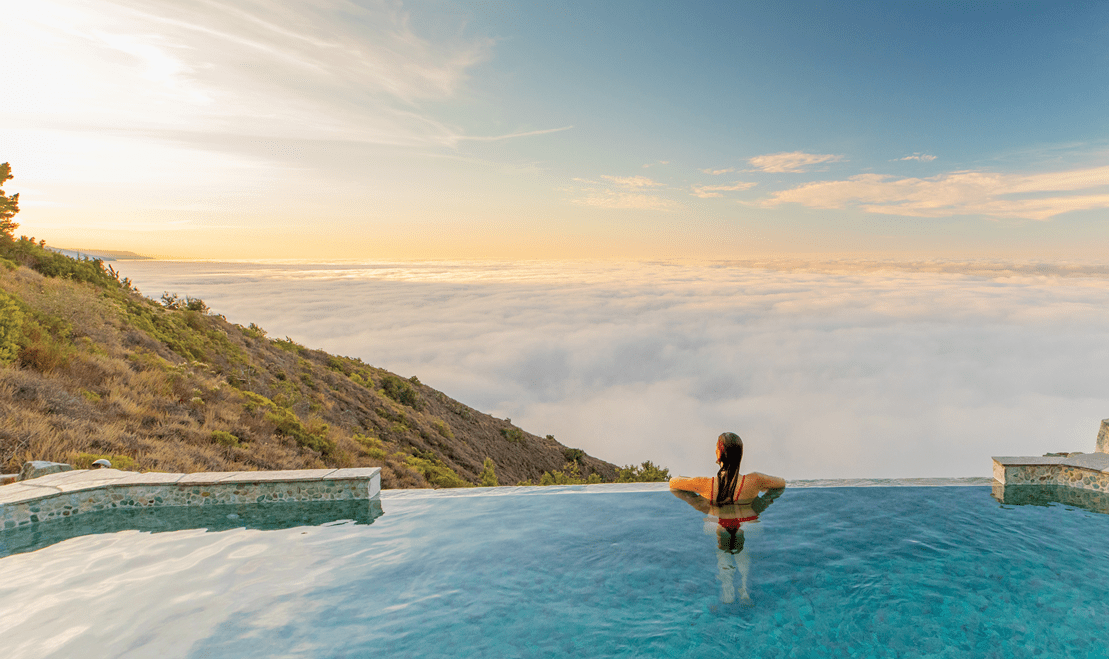 A woman looking over the beautiful skyline from an infinity pool at the Post Ranch Inn.