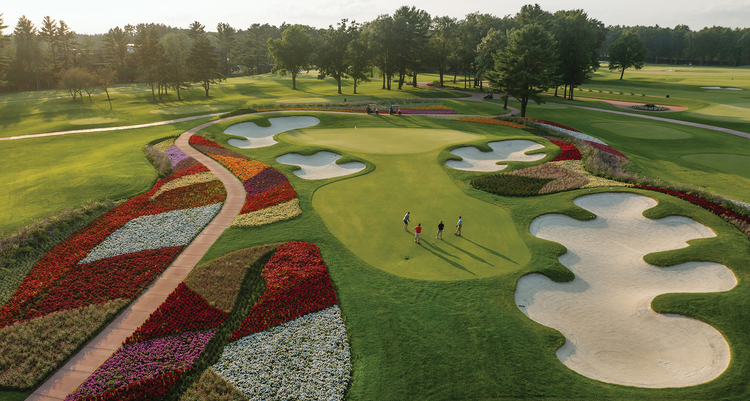 Four people golfing on the green at the 16th hole filled with colorful flowers at SentryWorld in Stevens Point, Wisconsin.