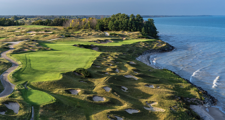 A winding golfing hole with fine cut greens and luscious trees in the background at Whistling Straits by Kohler.